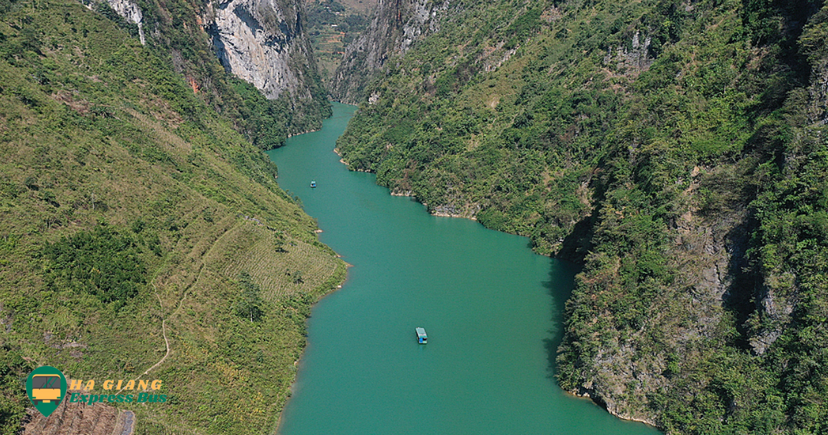 Crystal-clear waters of Nho Que River winding through steep rocky cliffs, surrounded by lush greenery under a blue sky